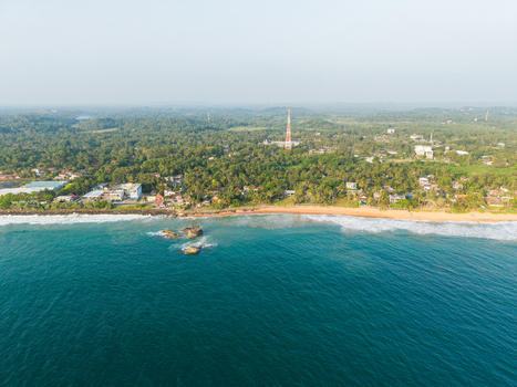 Aerial view of the tropical coastline with a sandy beach lush palm trees and a tall communication tower in Galle Southern Province Sri Lanka.
