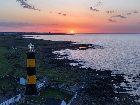 Aerial view of St. John s Point Lighthouse with its iconic black and yellow stripes standing on the rocky coastline during a vibrant sunset in Newcastle Northern Ireland United Kingdom. Aerial view of St. John s Point Lighthouse with its iconic black and yellow stripes standing on the rocky coastline during a vibrant sunset in Newcastle Northern Ireland United Kingdom.