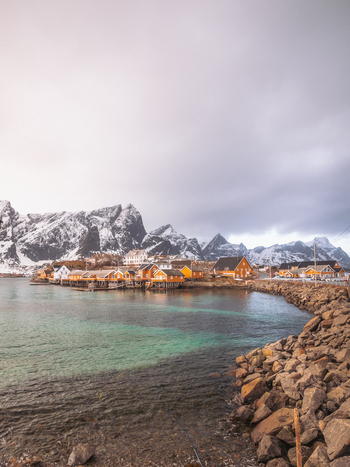 View of golden light kisses the quaint village nestled by the turquoise waters under snow dusted peaks a stone path leading into the tranquil scene Hamn&oslash;y Nordland Norway.