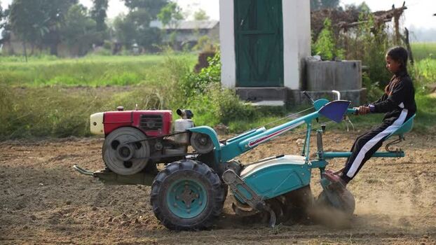 View of a young girl operating a power tiller in a field Nepal. View of a young girl operating a power tiller in a field Nepal.