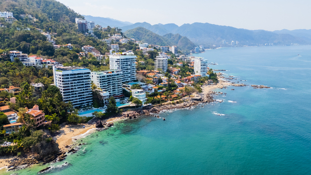 Aerial view of where emerald waters meet the sandy shore fringed by vibrant green hills dotted with buildings Puerto Vallarta Jalisco Mexico.