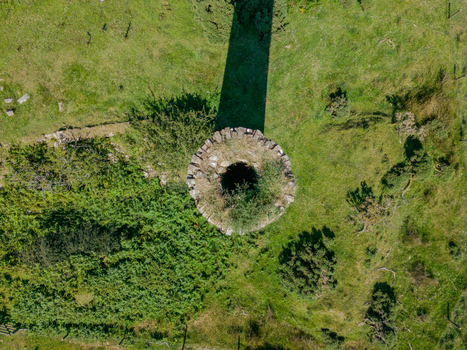 Aerial view of a historic circular stone mine engine house chimney surrounded by lush green grass and shrubs in Minions Cornwall United Kingdom. Aerial view of a historic circular stone mine engine house chimney surrounded by lush green grass and shrubs in Minions Cornwall United Kingdom.