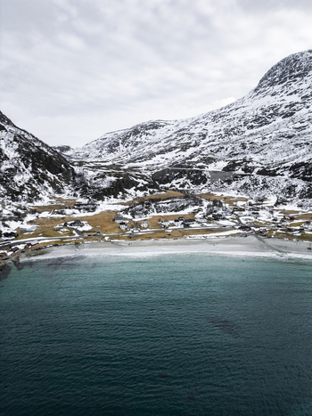 Aerial view of the Grotfjord beach and coastal village surrounded by majestic snow covered mountains and turquoise arctic waters in Tromvik Troms Norway. Aerial view of the Grotfjord beach and coastal village surrounded by majestic snow covered mountains and turquoise arctic waters in Tromvik Troms Norway.