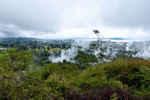 Aerial view of steam rising from the ground between houses and green fields under a cloudy sky Rotorua New Zealand. Aerial view of steam rising from the ground between houses and green fields under a cloudy sky Rotorua New Zealand.