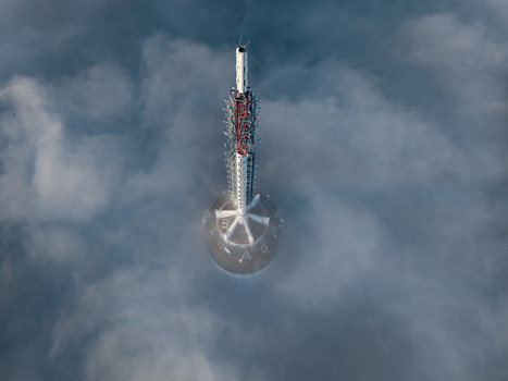 Aerial view of a tall telecommunications tower piercing through a thick layer of white clouds and fog under soft daylight Roermond Limburg Netherlands.