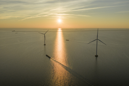 Aerial view of offshore wind turbines and a cargo ship sailing on the calm sea during a golden sunset in Netherlands. Aerial view of offshore wind turbines and a cargo ship sailing on the calm sea during a golden sunset in Netherlands.