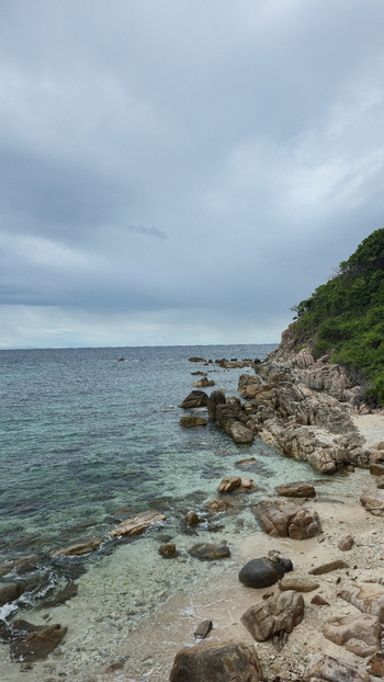 View of the rocky coastline of Ko Tao with turquoise water and lush green vegetation under a cloudy sky in Ko Tao Surat Thani Thailand.