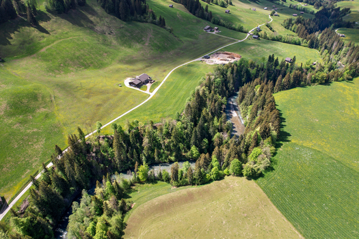 Aerial view of the Sarine river winding through lush green meadows and dense pine forests with traditional alpine chalets Rougemont Vaud Switzerland. Aerial view of the Sarine river winding through lush green meadows and dense pine forests with traditional alpine chalets Rougemont Vaud Switzerland.