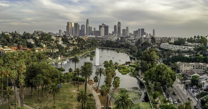 Aerial view of Echo Park Lake with its fountain surrounded by palm trees and greenery with the downtown Los Angeles skyline in the distance Los Angeles CA United States. Aerial view of Echo Park Lake with its fountain surrounded by palm trees and greenery with the downtown Los Angeles skyline in the distance Los Angeles CA United States.