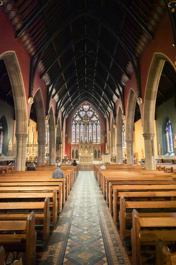 View of the interior of St. Mary s Cathedral featuring wooden pews stone arches and a stained glass window in Newcastle upon Tyne England United Kingdom. View of the interior of St. Mary s Cathedral featuring wooden pews stone arches and a stained glass window in Newcastle upon Tyne England United Kingdom.