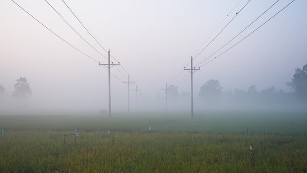 View of power lines in a foggy field in Bangladesh.