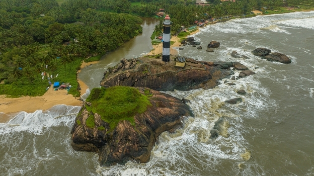 Aerial view of Kapu Light House situated on a rocky outcrop surrounded by crashing waves and lush palm trees along the coastline in Udupi Karnataka India.