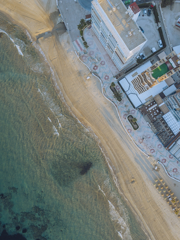 Aerial view of the sandy beach and coastal promenade featuring modern apartment buildings palm trees and clear turquoise waters in Calp Valencian Community Spain. Aerial view of the sandy beach and coastal promenade featuring modern apartment buildings palm trees and clear turquoise waters in Calp Valencian Community Spain.