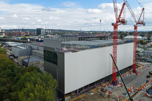 Aerial view of a large data center under construction with red tower cranes steel framework and modern facade panels in the United Kingdom.