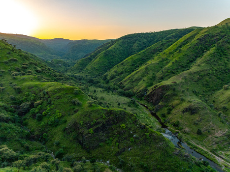 Aerial view of a lush green valley with a winding stream flowing through the hills during golden hour in Udaipur Rajasthan India.