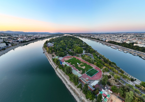 Aerial view of Margaret Island s athletics track and tree lined park between the Danube branches with docked riverboats and central Budapest at sunset Hungary. Aerial view of Margaret Island s athletics track and tree lined park between the Danube branches with docked riverboats and central Budapest at sunset Hungary.