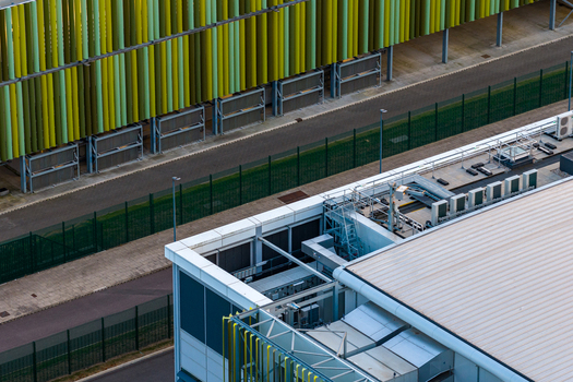 Aerial view of the Kao Data campus featuring modern industrial architecture green and yellow facades rooftop HVAC units and perimeter fencing in Harlow England United Kingdom. Aerial view of the Kao Data campus featuring modern industrial architecture green and yellow facades rooftop HVAC units and perimeter fencing in Harlow England United Kingdom.