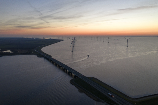 Aerial view of Ketelbrug bridge spanning across the water with offshore wind turbines and a boat under a sunset sky in Nagele Flevoland Netherlands.