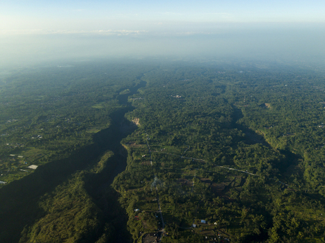 Aerial view of Kali Gendol river valley cutting through dense tropical forest and lush green vegetation under a clear morning sky Cangkringan Special Region of Yogyakarta Indonesia.