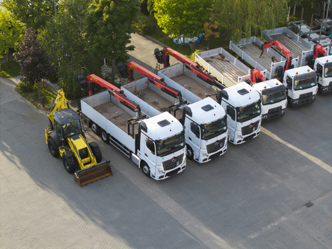 Krakow Poland 16 September 2026 Aerial view of a fleet of white Mercedes Benz trucks with red cranes parked in a row next to a yellow backhoe loader at the CIEZAROWKI.PL facility.