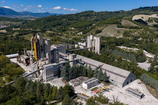 Aerial view of the Sacci S.P.A. cement factory featuring industrial silos and processing structures surrounded by green hills in Castelraimondo Marche Italy. Aerial view of the Sacci S.P.A. cement factory featuring industrial silos and processing structures surrounded by green hills in Castelraimondo Marche Italy.