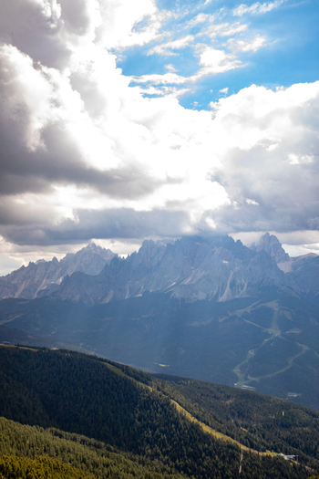 View of the jagged peaks of the Dolomites under dramatic white clouds and a blue sky above forested mountain slopes in Rocca Pietore Veneto Italy. View of the jagged peaks of the Dolomites under dramatic white clouds and a blue sky above forested mountain slopes in Rocca Pietore Veneto Italy.
