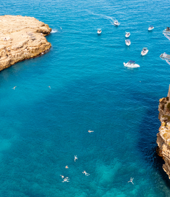Aerial view of the turquoise waters of Lama Monachile beach with small boats and swimmers near the rocky cliffs of Polignano a Mare Apulia Italy.