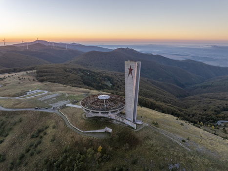 Aerial view of the abandoned Buzludzha Monument perched on a mountain peak at sunset with wind turbines in the distance in Stara Zagora Bulgaria. Aerial view of the abandoned Buzludzha Monument perched on a mountain peak at sunset with wind turbines in the distance in Stara Zagora Bulgaria.