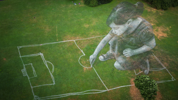 Aerial view of a massive girl image drawing a football field on the bright green grass a whimsical contrast of scale and artistry Gen&egrave;ve Gen&egrave;ve Switzerland.