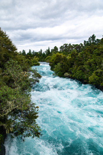 View of the Huka Falls turquoise waters surging powerfully through the lush green landscape under a cloudy sky Huka Falls Waikato Region New Zealand. View of the Huka Falls turquoise waters surging powerfully through the lush green landscape under a cloudy sky Huka Falls Waikato Region New Zealand.