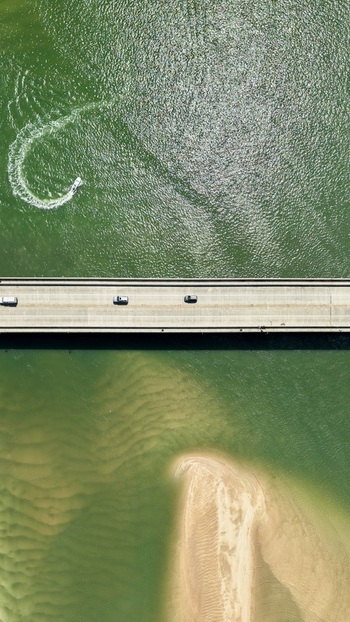 Aerial view of Matanzas Inlet showing the bridge with cars crossing a small boat leaving a wake in the green water and a sandy shoal in St. Johns County Florida United States. Aerial view of Matanzas Inlet showing the bridge with cars crossing a small boat leaving a wake in the green water and a sandy shoal in St. Johns County Florida United States.
