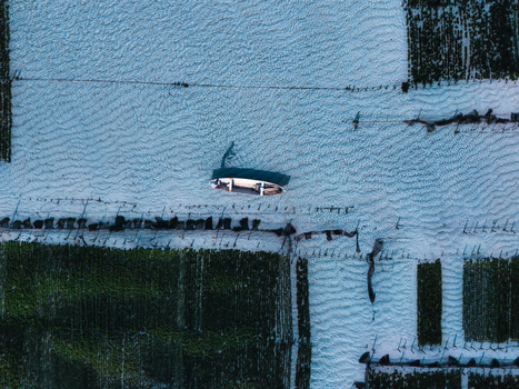 Aerial view of a boat adrift on the shimmering rippled sea nestled among the verdant seaweed farms Lembongan Bali Indonesia. Aerial view of a boat adrift on the shimmering rippled sea nestled among the verdant seaweed farms Lembongan Bali Indonesia.