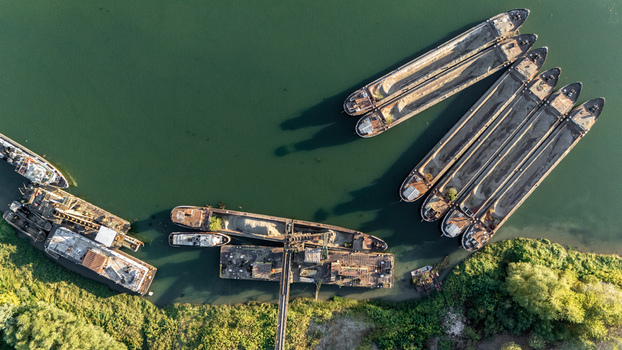 Aerial view of cargo barges moored on the Sava River with industrial loading equipment and lush green riverbanks in Sremska Mitrovica Vojvodina Serbia.