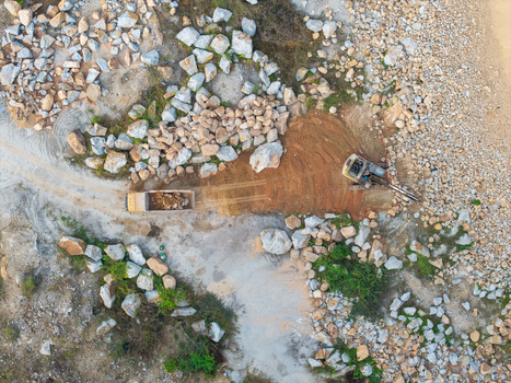 Aerial view of a mining site with an excavator loading rocks into a dump truck surrounded by piles of stone and gravel in Bukit Tambun Penang Malaysia. Aerial view of a mining site with an excavator loading rocks into a dump truck surrounded by piles of stone and gravel in Bukit Tambun Penang Malaysia.