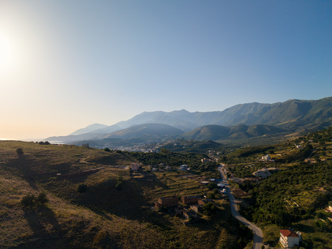 Aerial view of rolling green hills and a winding road leading through a mountainous landscape under a clear sky in Porto Palermo Qarku i Vlores Albania. Aerial view of rolling green hills and a winding road leading through a mountainous landscape under a clear sky in Porto Palermo Qarku i Vlores Albania.