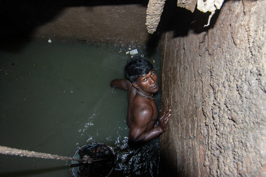 Dhaka Bangladesh 18 April 2018 View of a sewer cleaner working inside a narrow manhole filled with murky water and debris. Dhaka Bangladesh 18 April 2018 View of a sewer cleaner working inside a narrow manhole filled with murky water and debris.