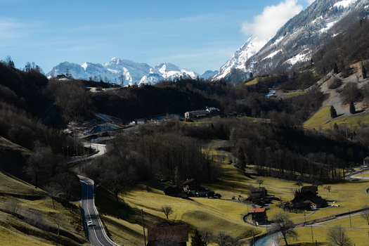 View of winding roads carve through green valleys beneath snow capped mountains a serene journey captured in Switzerland Train from Lucerne to Interlaken Switzerland. View of winding roads carve through green valleys beneath snow capped mountains a serene journey captured in Switzerland Train from Lucerne to Interlaken Switzerland.