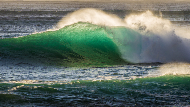 View of a powerful turquoise ocean wave breaking at the North Shore during golden hour with sunlight illuminating the crest and sea spray in Haleiwa Hawaii United States.