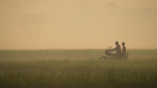 View of a motorcycle riding through a misty field Bangladesh.