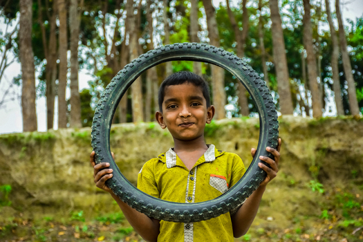 Kushtia Bangladesh 12 March 2020 View of a young boy holding a bicycle tire frame around his face in a rural setting. Kushtia Bangladesh 12 March 2020 View of a young boy holding a bicycle tire frame around his face in a rural setting.
