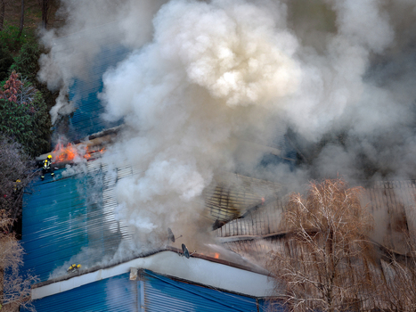 Aerial view of a building fire with thick smoke billowing from a blue roof as a firefighter works to extinguish the flames in Belgrade City of Belgrade Serbia. Aerial view of a building fire with thick smoke billowing from a blue roof as a firefighter works to extinguish the flames in Belgrade City of Belgrade Serbia.