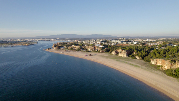 Aerial view of the sandy beach and rugged cliffs of Ferragudo with the town and calm blue waters of the Arade River estuary in Ferragudo Faro District Portugal.
