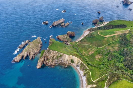 Aerial view of Silence Beach Viewpoint featuring dramatic cliffs rocky islets and lush green hills along the coast in Cudillero Asturias Spain.