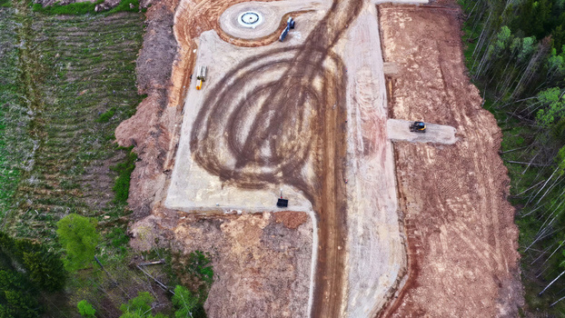 Aerial view of a wind turbine foundation construction site featuring a circular concrete base heavy machinery tire tracks in the soil and surrounding forest in Latvia. Aerial view of a wind turbine foundation construction site featuring a circular concrete base heavy machinery tire tracks in the soil and surrounding forest in Latvia.