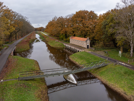 Aerial view of a canal reflecting the overcast sky flowing past the Harseveldweg and a small building lined by trees Tilligte Overijssel Netherlands. Aerial view of a canal reflecting the overcast sky flowing past the Harseveldweg and a small building lined by trees Tilligte Overijssel Netherlands.