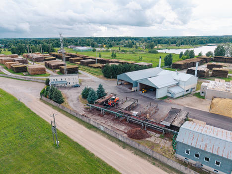 Aerial view of a lumber mill facility featuring large stacks of logs industrial processing buildings and heavy machinery in a rural landscape in Brankas Jelgava Municipality Latvia. Aerial view of a lumber mill facility featuring large stacks of logs industrial processing buildings and heavy machinery in a rural landscape in Brankas Jelgava Municipality Latvia.