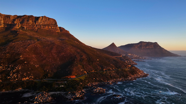 Aerial view of the rugged Twelve Apostles mountain range and winding coastal road along the Atlantic Ocean at sunset in Cape Town Western Cape South Africa. Aerial view of the rugged Twelve Apostles mountain range and winding coastal road along the Atlantic Ocean at sunset in Cape Town Western Cape South Africa.