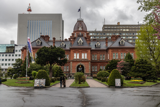 View of the historic Former Hokkaido Government Office with its distinctive red brick facade and central dome surrounded by lush gardens and modern city buildings in Sapporo Hokkaido Japan. View of the historic Former Hokkaido Government Office with its distinctive red brick facade and central dome surrounded by lush gardens and modern city buildings in Sapporo Hokkaido Japan.