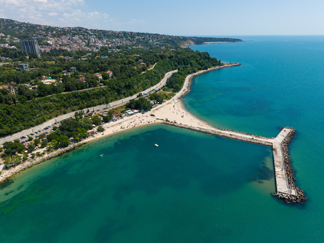 Aerial view of Alley First beach with its long concrete pier extending into the Black Sea surrounded by lush green coastal cliffs and urban development in Varna Varna Bulgaria. Aerial view of Alley First beach with its long concrete pier extending into the Black Sea surrounded by lush green coastal cliffs and urban development in Varna Varna Bulgaria.