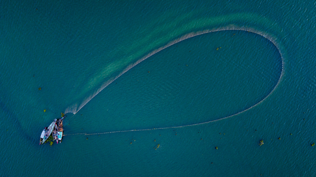 Aerial view of a traditional fishing boat with a large circular net spread across the deep blue waters of Kaptai Lake in Rangamati Chittagong Division Bangladesh.